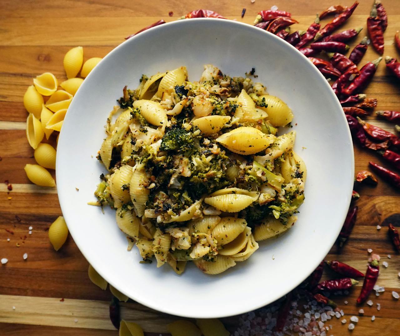 A tempting bowl of shell pasta mixed with broccoli and chili peppers on a rustic wooden table.